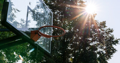plastic backboard with red hoop on basketball playground under bright rays of sun