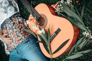 Close-up picture of acoustic guitar is on the grass and young hippie women wearing boho style...