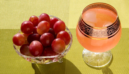 Grapes in a crystal vase with grape juice with ice on a bright green background.
