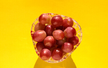 Grapes in a crystal vase on a bright yellow background.