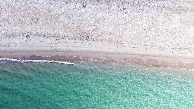 SOS message written on sand beach by blue sea splashing the coast. Help on the beach.Aerial view 