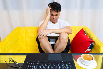 headache, tense young asian man working on laptop computer in living room at night