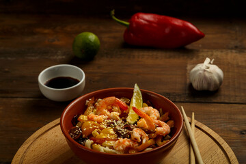 udon with mushrooms and shrimps in a clay plate on a round stand next to chopsticks and ingredients.