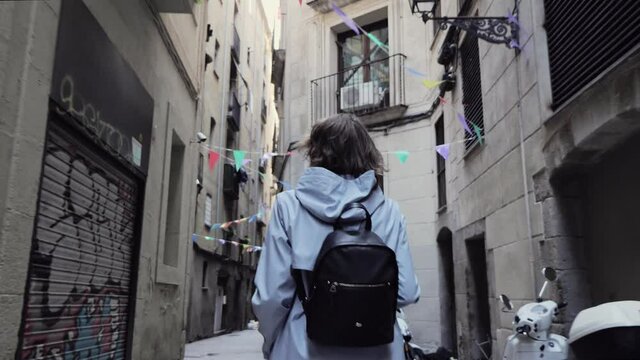Back view of a girl with backpack walking through tight street. Enjoying of city architecture. Girl holding a camera in the hands