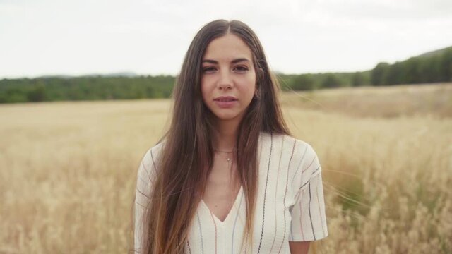 Portrait Of A Beautiful Girl Standing On The Crop Fields Looking Straight At The Camera. - medium shot