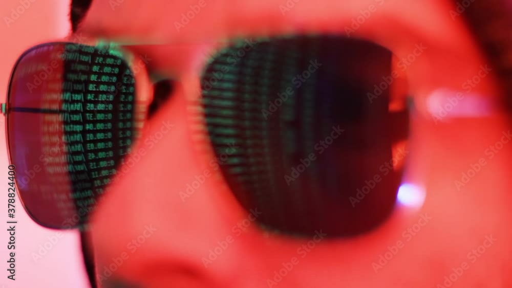 Poster male hacker looking at computer code with mirror screen reflection on sunglasses close up