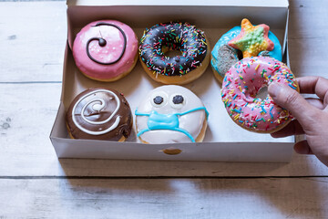 a hand picking up a donuts from a box. handmade donuts with face mask due to covid pandemic