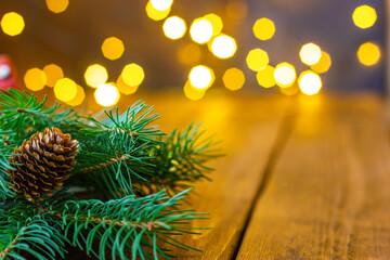 Fir branches with a pine cone on a wooden dark table. In the background there is a bokeh of Christmas lights. On the right is a place to insert an item or text.