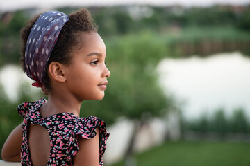 Portrait of a beautiful mixed race kid on a landscape background. Beautiful profile. Soft light. Afro hair. The child looks to the right. Concept of childhood, travel, dreams. Copy space. Horizontal.