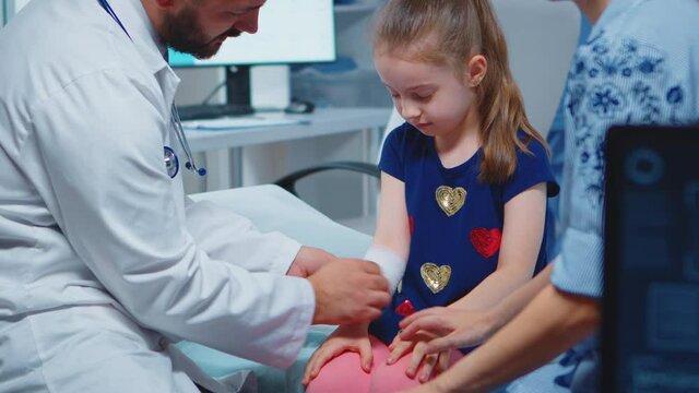 Little girl having arm bandaged sitting in bed during consultation. Healthcare physician specialist in medicine providing health care service radiographic treatment examination in hospital cabinet