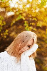 Portrait of young teenage blonde girl in white sweater on autumn background. Posing, outdoor and fall concept.