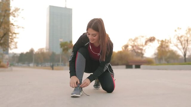 Sporty woman tying running shoes in urban park.	
