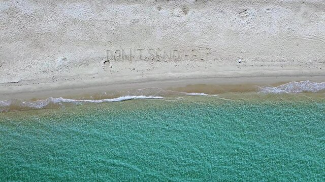 Aerial view of sand beach with Don't send help message and blue sea splashing the beach 