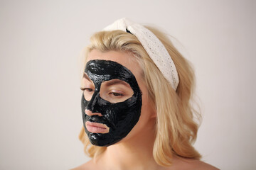 Beautiful blonde woman with a cleansing black mask on her face.