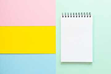Spiral notebook with blank white sheet on multi-colored paper. The concept of office, school, creativity, learning. Top view, flat lay, copy space, minimalism. Pink, blue and yellow shades.
