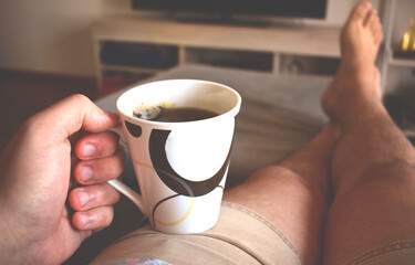 Hand holding a cup of tea on a gray armchair