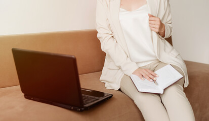 Naklejka premium Woman using laptop, sitting on the sofa, close-up photo of female hands, notebook and laptop