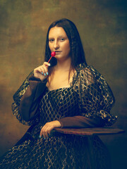 Candy. Young woman as Mona Lisa, La Gioconda isolated on dark green background. Retro style, comparison of eras concept. Beautiful female model like classic historical character, old-fashioned.