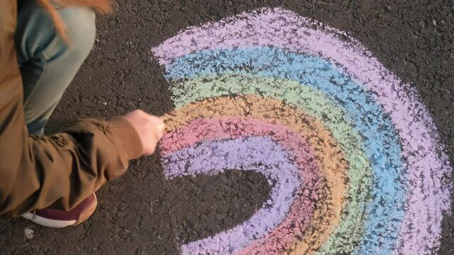 little girl painting a rainbow on the asphalt