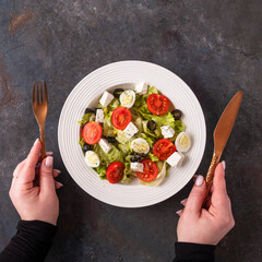 Colorful vegetables with quail eggs and cheese on a plate. Female hands holds fork and knife. Diet concept. Top view