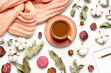 Flat lay autumn composition. Cup of coffee pink knitted women's sweater or warm plaid cotton flowers dry rose eucalyptus macaroon cake blank notebook pencil on white background top view. Fall concept