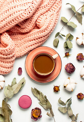 Flat lay autumn composition. Cup of coffee pink knitted women's sweater or warm plaid cotton flowers dry rose eucalyptus macaroon cake blank notebook pencil on white background top view. Fall concept
