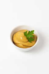 Mustard sauce decorated with parsley in a small white bowl on a white background