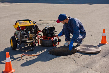 Plumber diagnoses a drain well on the street using special equipment. - obrazy, fototapety, plakaty