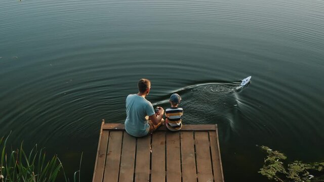 Father and little son play with RC toy speedboat on the lake. Playing with my son in nature