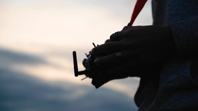 The guy holds the drone control panel in his hands. The evening sky is in the background