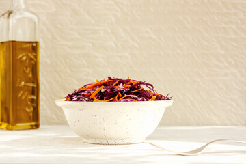 Vitamin red cabbage salad with carrot and bean sprouts in a boal and bottle of oil on light background. Healthy eating, vegan food concept