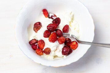 Red juicy wild strawberries with cottage cheese and sour cream in bowl with spoon