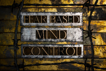 Fear Based Mind Control text formed with real authentic typeset letters with barbed wire on vintage textured silver grunge copper and gold background