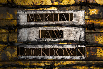 Martial Law Lockdown text formed with real authentic typeset letters with barbed wire on vintage textured silver grunge copper and gold background