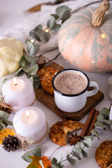 Hot cocoa with cookies in a white mug surrounded by autumn leaves and pumpkins