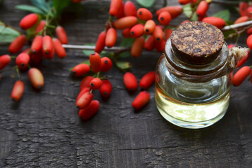 Barberry essential oil in a glass bottle on old wooden table for aromatherapy,skin care or spa.Berberis vulgaris herb extract.Selective focus.