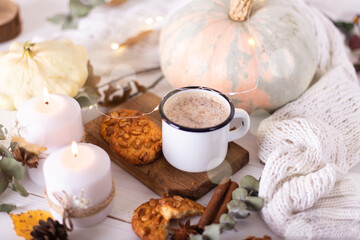 Hot cocoa with cookies in a white mug surrounded by autumn leaves and pumpkins