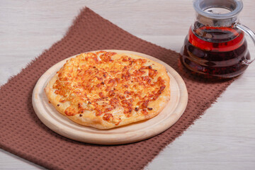 A round pie in the with Circassian cheese and Suluguni cheese is on the wooden background with brown napkin. Served with  tea.