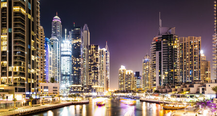Stunning view of the Dubai Marina at dusk with illuminated skyscrapers in the background and light trails left by some boats sailing in the water canal. Dubai, United Arab Emirates.