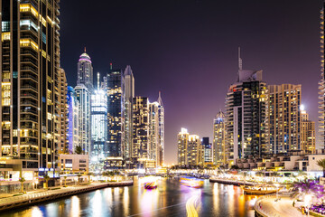 Fototapeta na wymiar Stunning view of the Dubai Marina at dusk with illuminated skyscrapers in the background and light trails left by some boats sailing in the water canal. Dubai, United Arab Emirates.