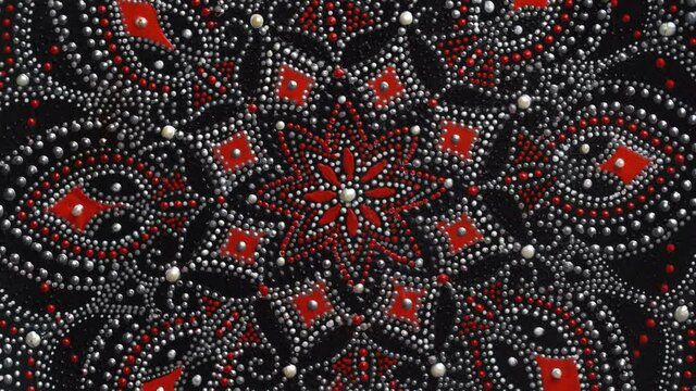 Decorative ceramic plate with red and silver colors, painted plate rotating on background, closeup, top view. Decorative porcelain plate painted with acrylic paints, handwork, dot painting