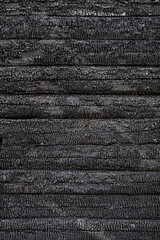 Texture (background, pattern) of a charred log wall of a burned-out wooden house. Vertical image.