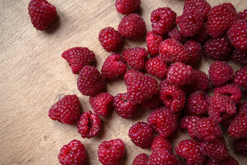 Red ripe raspberries are scattered on a wooden table. Raspberries