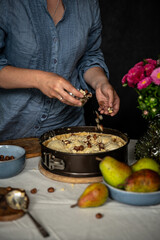 Step by step process of making frangipani tart with pear, hazelnuts and chocolate. Adding hazelnuts. 