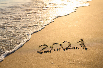 Inscription 2021 on the seashore. Beach and sea wave at sunset. Concept of the new 2021.