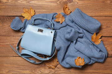 Warm sweater, bag and dry leaves on wooden background, flat lay. Autumn season