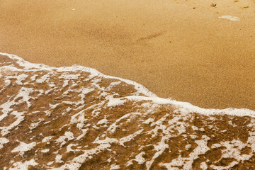 Soft wave of the sea on the sand beach with sunlight. Tropical sandy beach background with copy space. Top down view..
