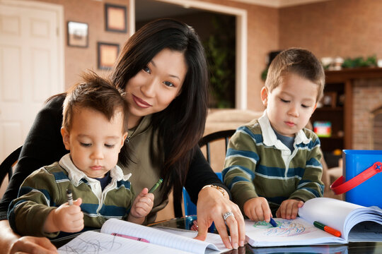 Asian mother watching sons draw with crayons