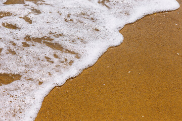 Soft wave of the sea on the sand beach with sunlight. Tropical sandy beach background with copy space. Top down view.