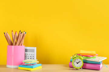 Fototapeta premium Different school stationery and alarm clock on table against yellow background, space for text. Back to school